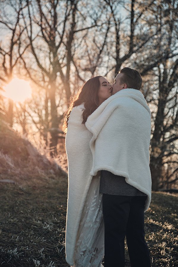 Eloping couple gets warm under blanket during winter elopement