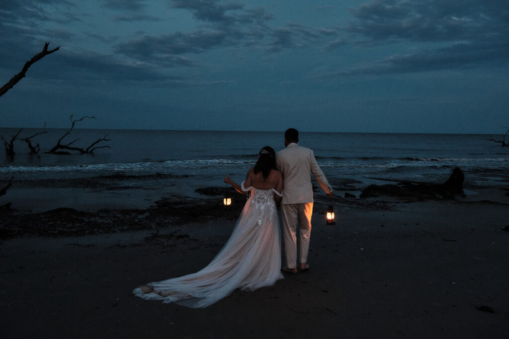 Couple holding lanterns looking out at the ocean during an elopement