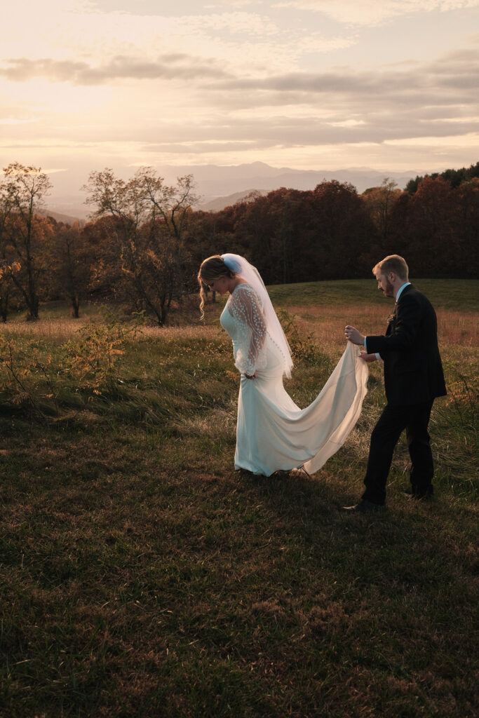 Groom holds a brides dress during sunset overlooking the mountains.