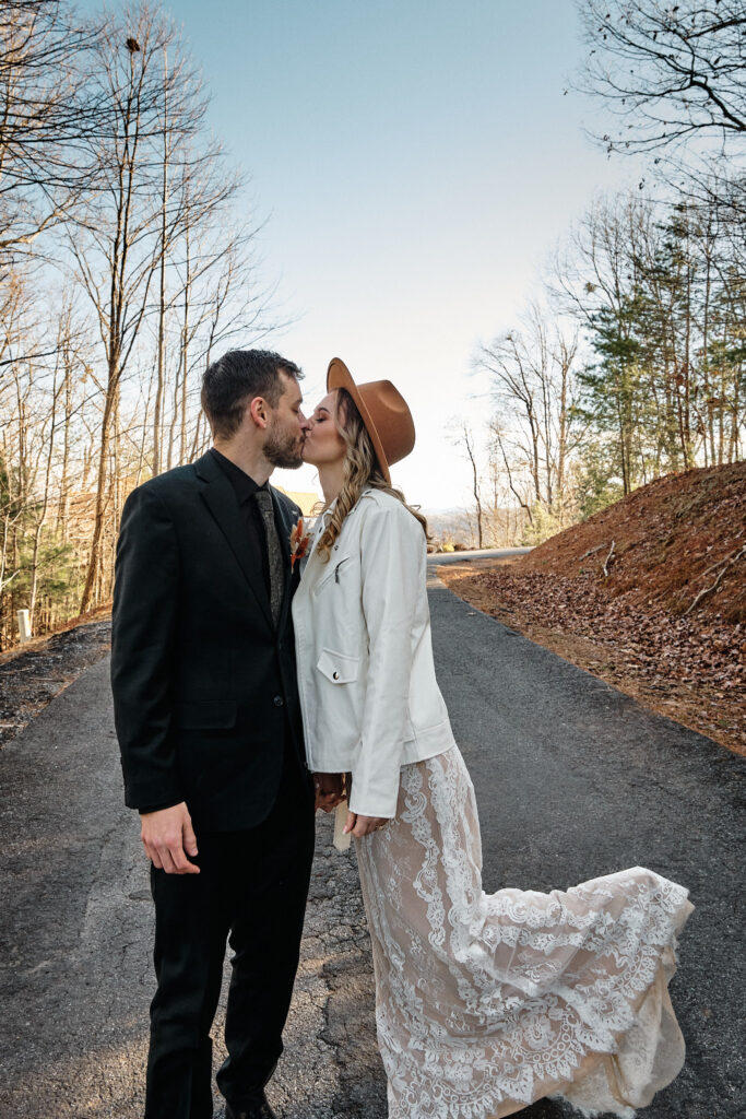 Eloping couple kissing along a forest road.