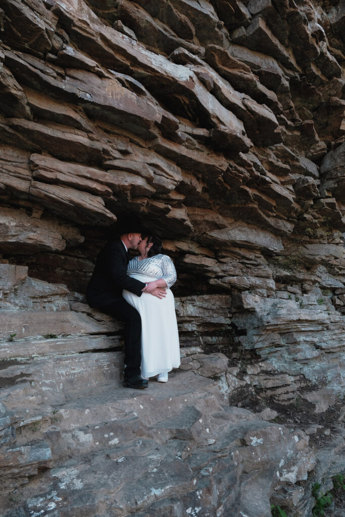 Eloping couple kissing within the rock formations of a cliff.