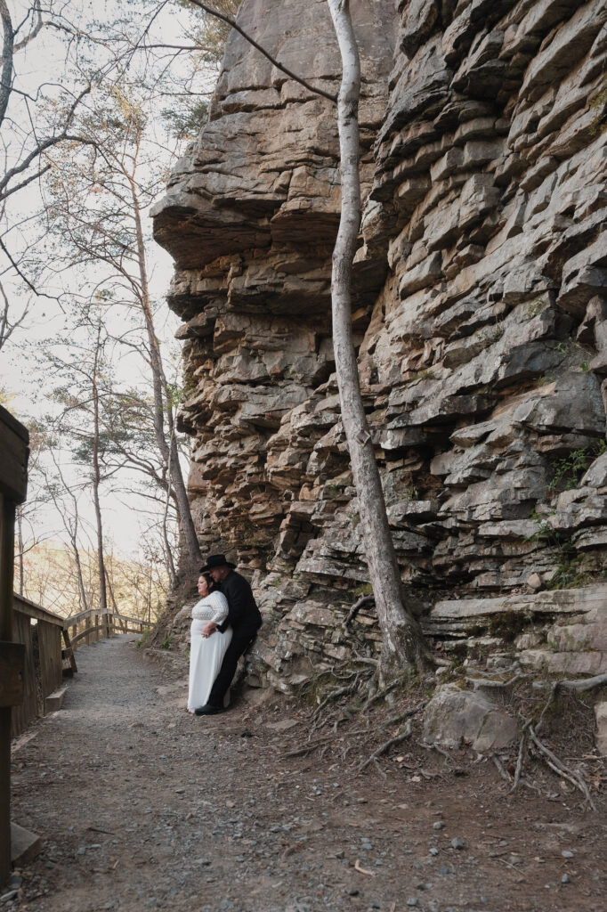 Eloping couple leaning against the base of cliff looking out into the distance.