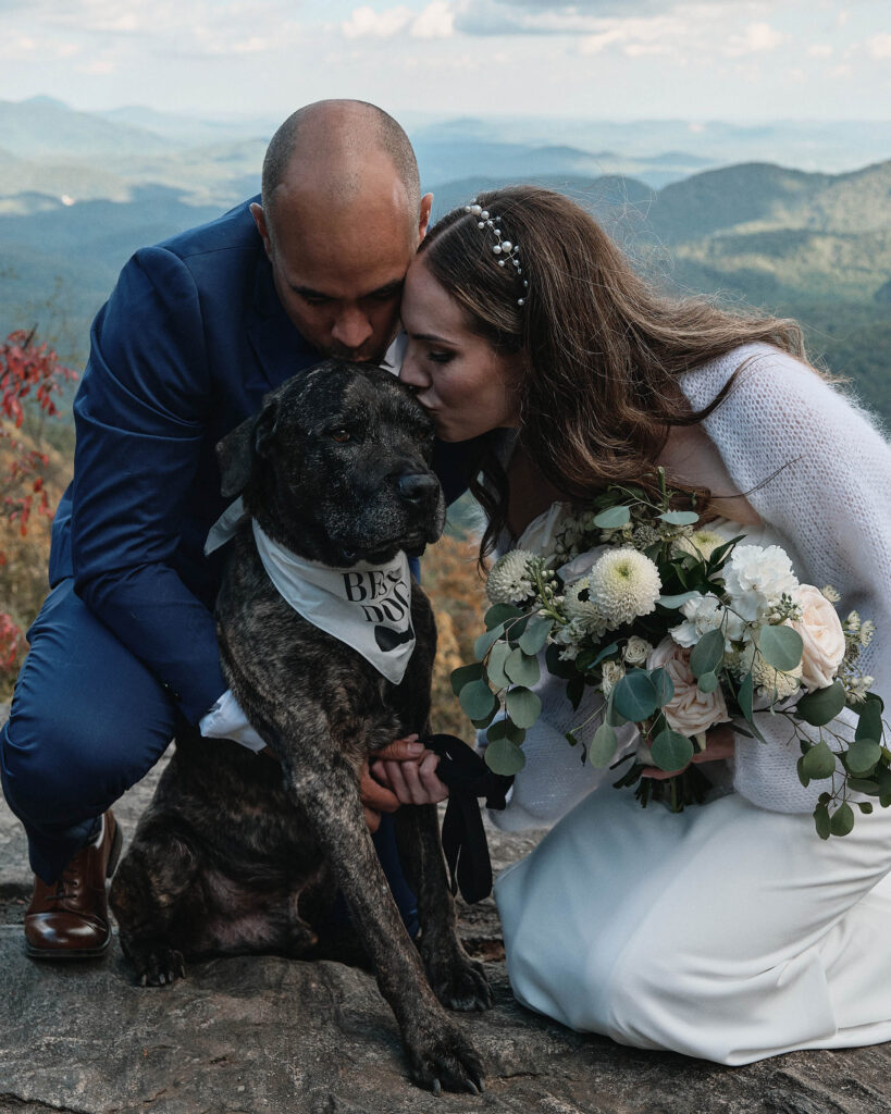 Hiking eloping couple kisses their dog in his best dog attire