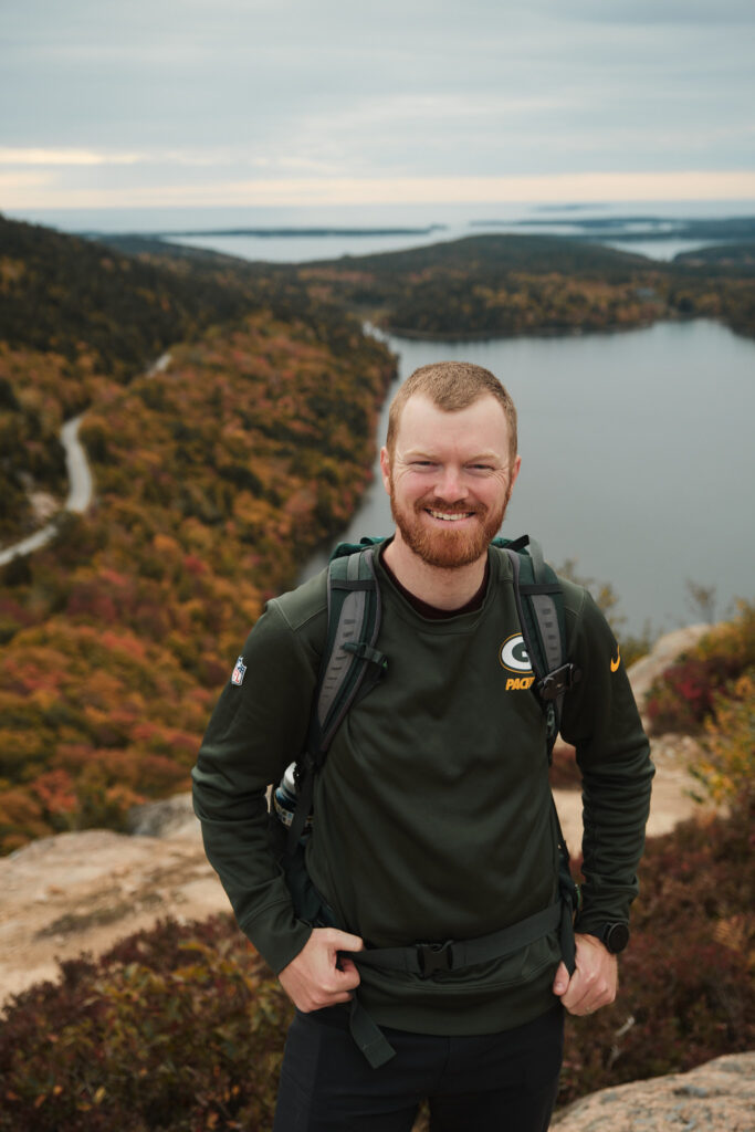 Elopement Photographer stands on top of a mountain smiling