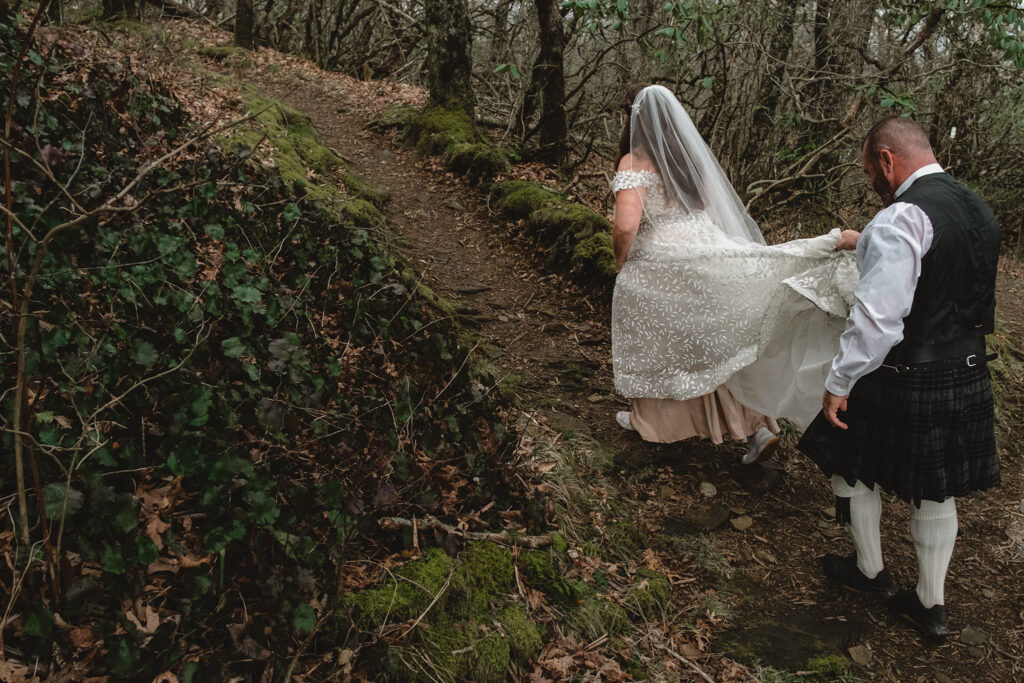 Groom helps bride hike along the trail by picking up her dress